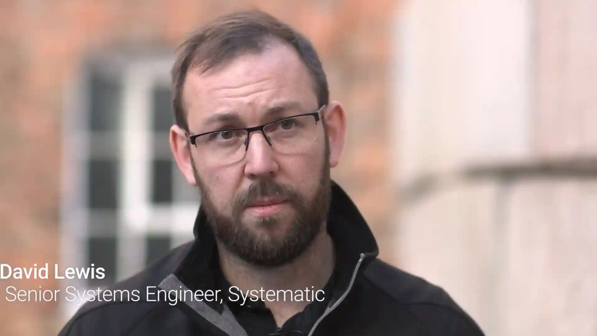 David Lewis, Senior Systems Engineer at Systematic, speaking outdoors in front of a building.