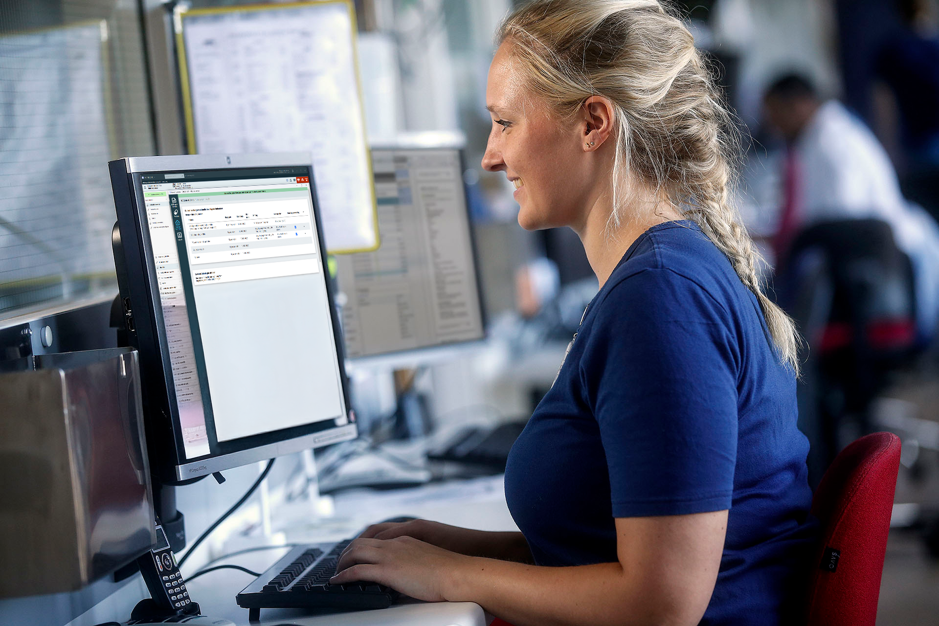 Sygeplejerske arbejder ved en computer med sundhedssoftware i et moderne klinisk miljø og håndterer patientdata.