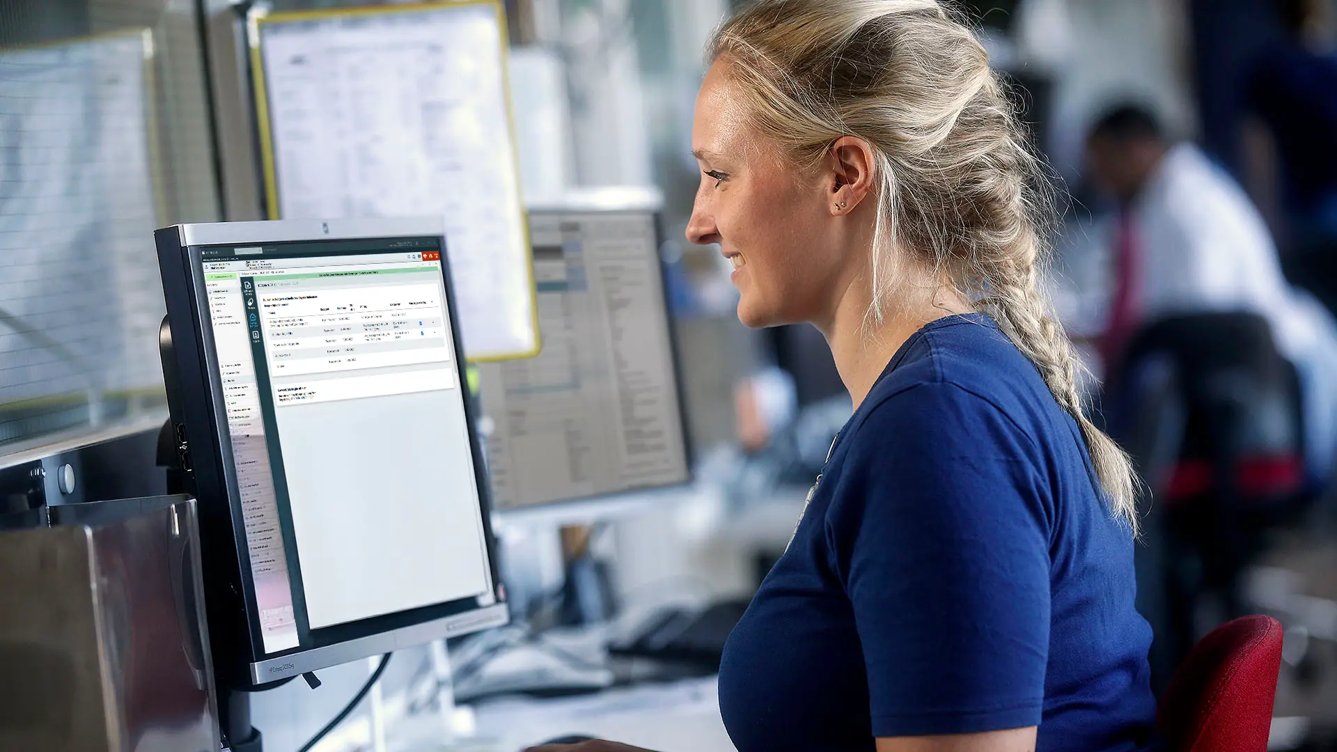 Nurse works at a computer using healthcare software in a modern clinical environment, focused on patient data management.