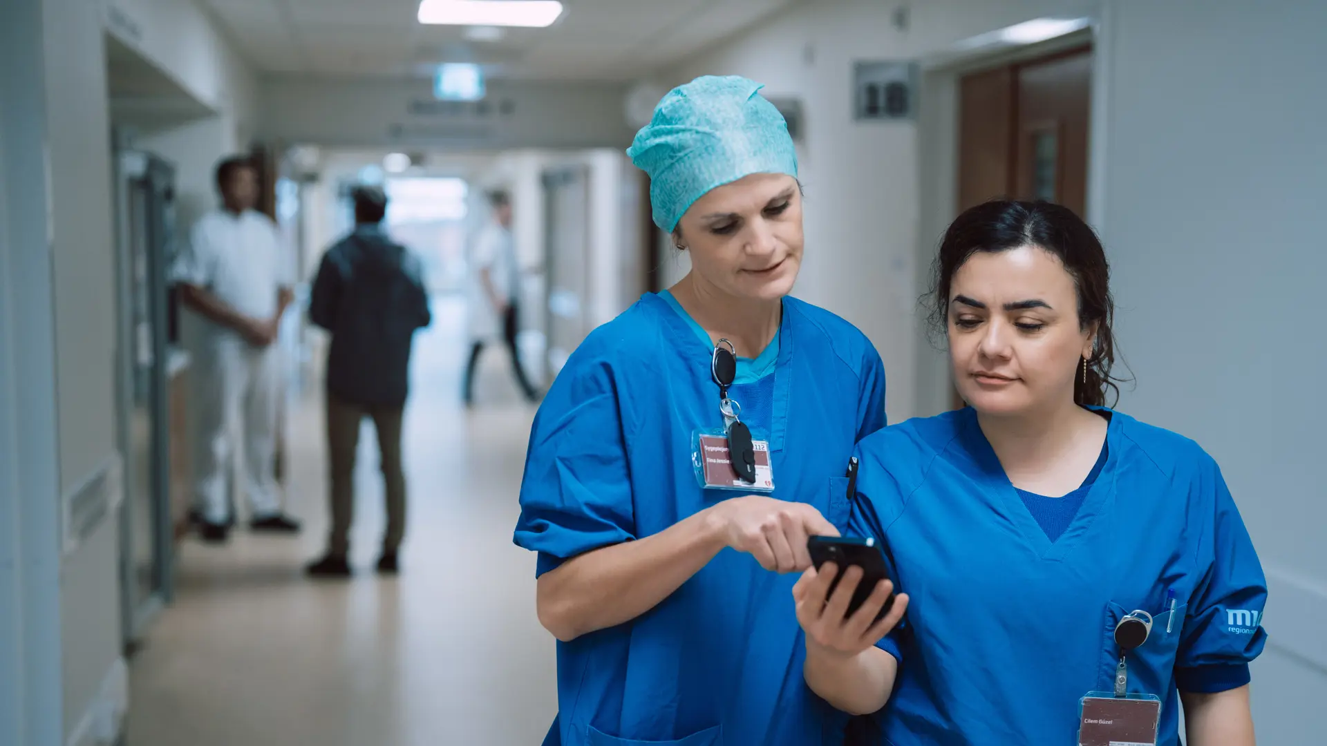 Nurses Looking At Columna Flow on Phone In Hospital Hallway