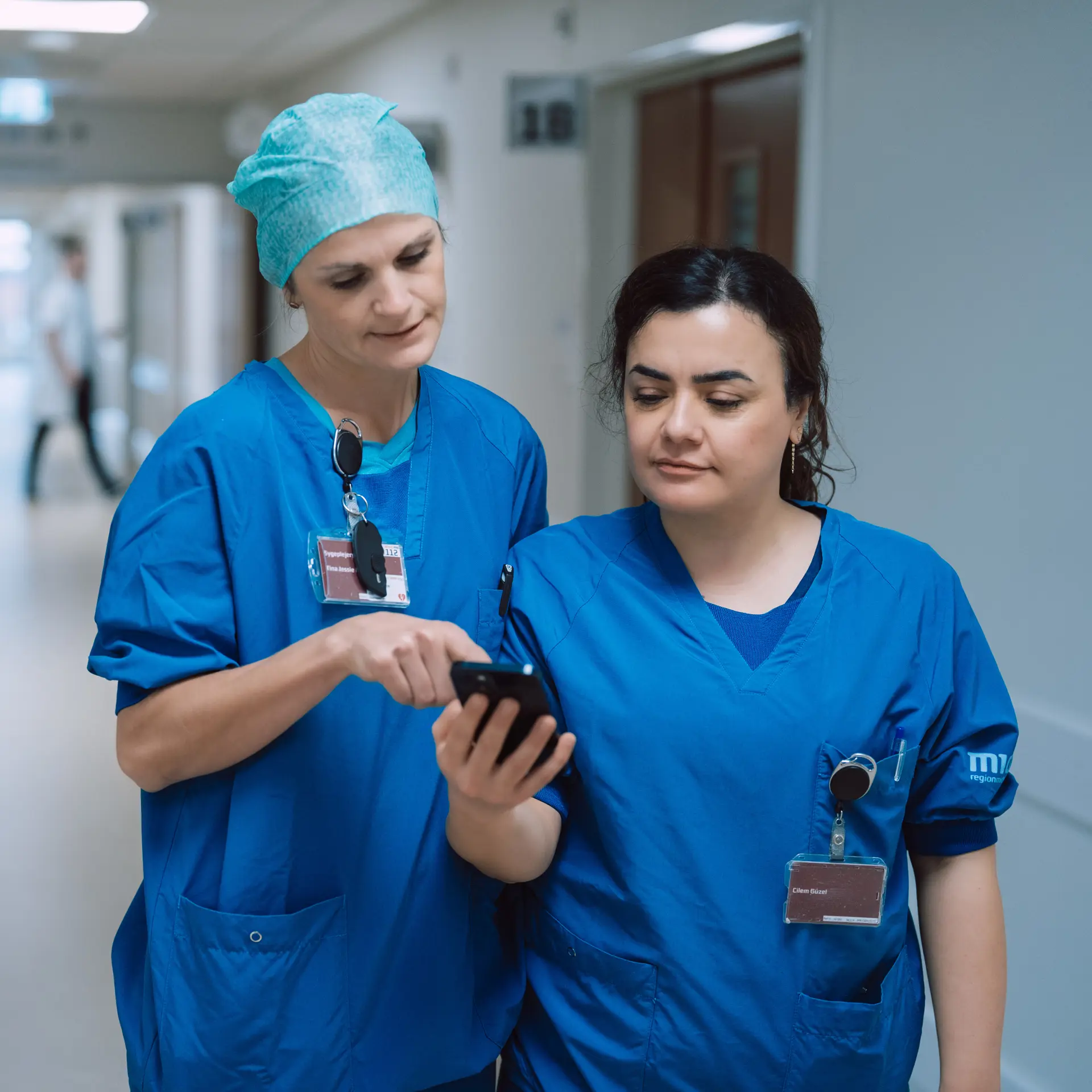 Nurses Looking At Columna Flow on Phone In Hospital Hallway