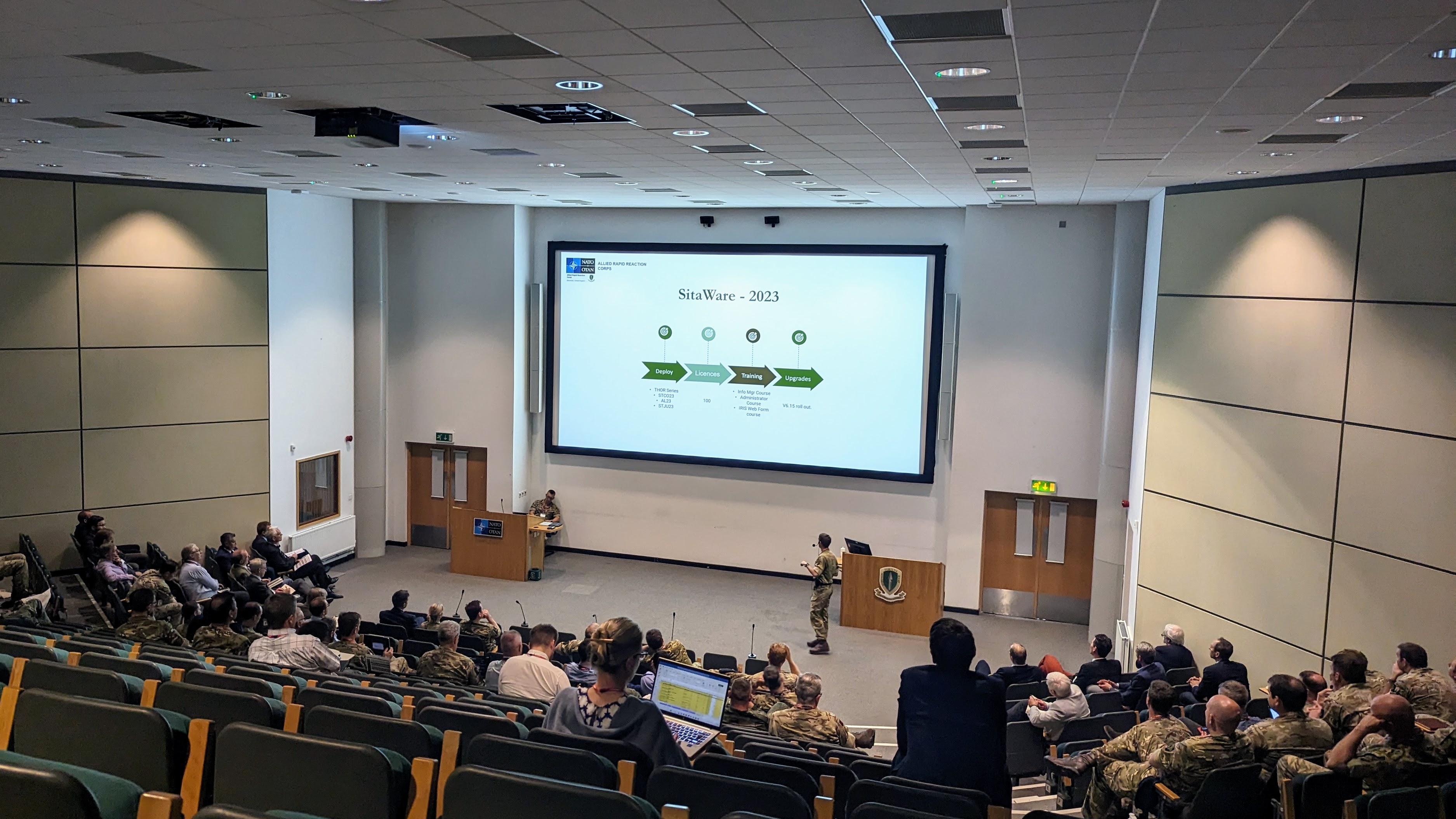 Military and defense professionals attend the SitaWare User Forum in the UK, listening to a presentation in a large auditorium.