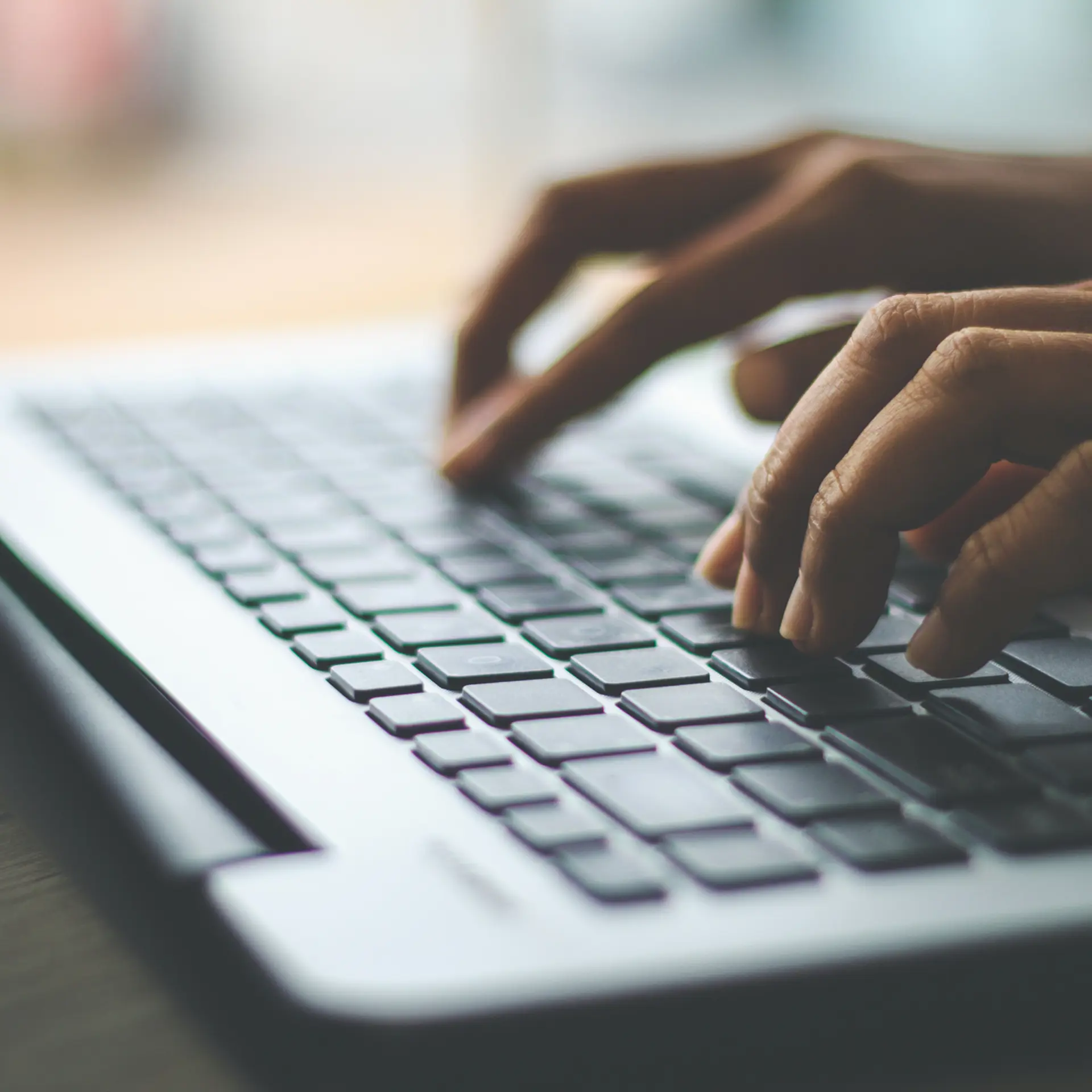 Nahaufnahme von Händen, die auf einer Laptop-Tastatur in einer hellen Arbeitsumgebung tippen.