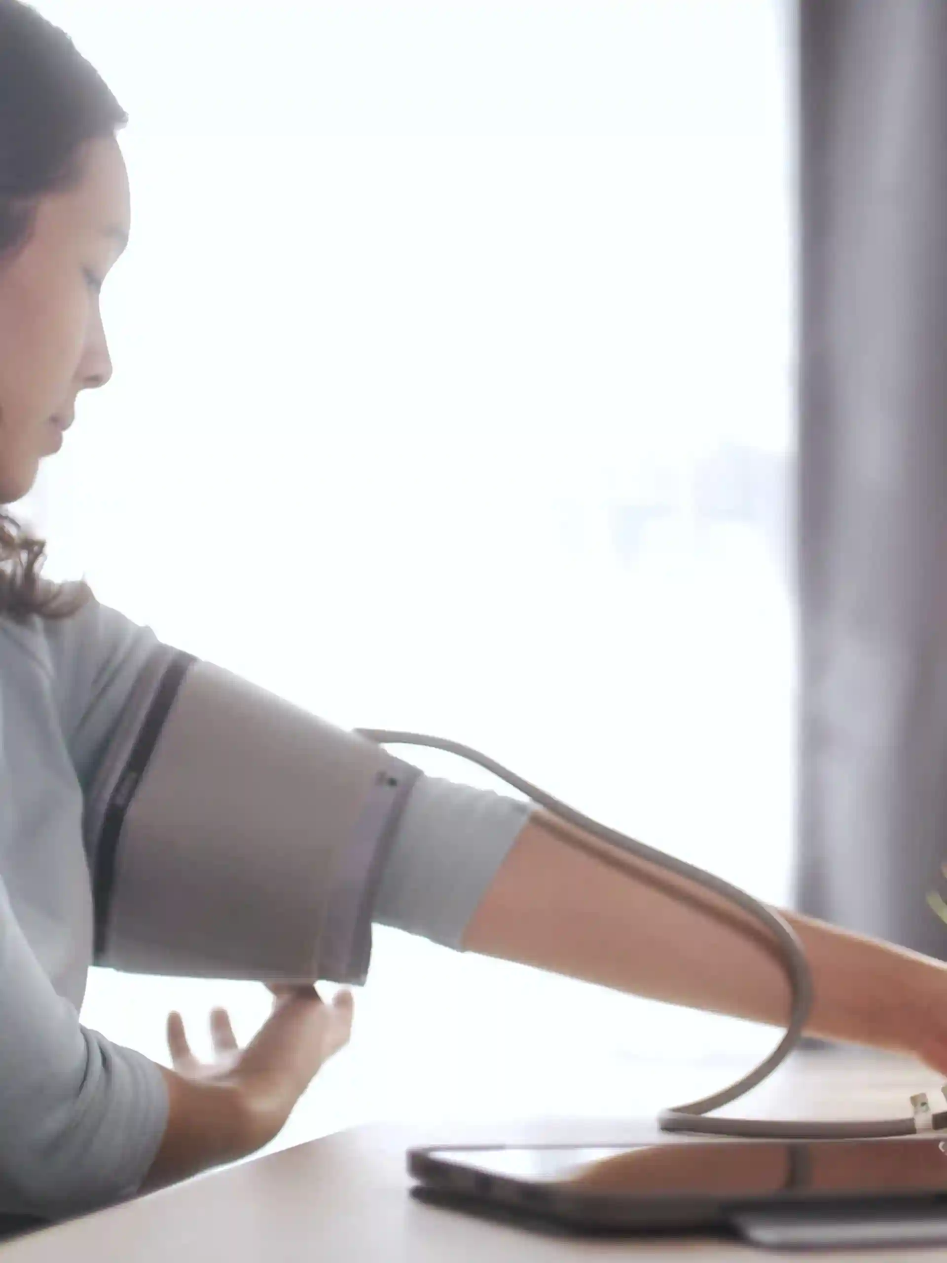 Woman measures her blood pressure at home using a digital monitor, illustrating personal health monitoring and remote care practices.