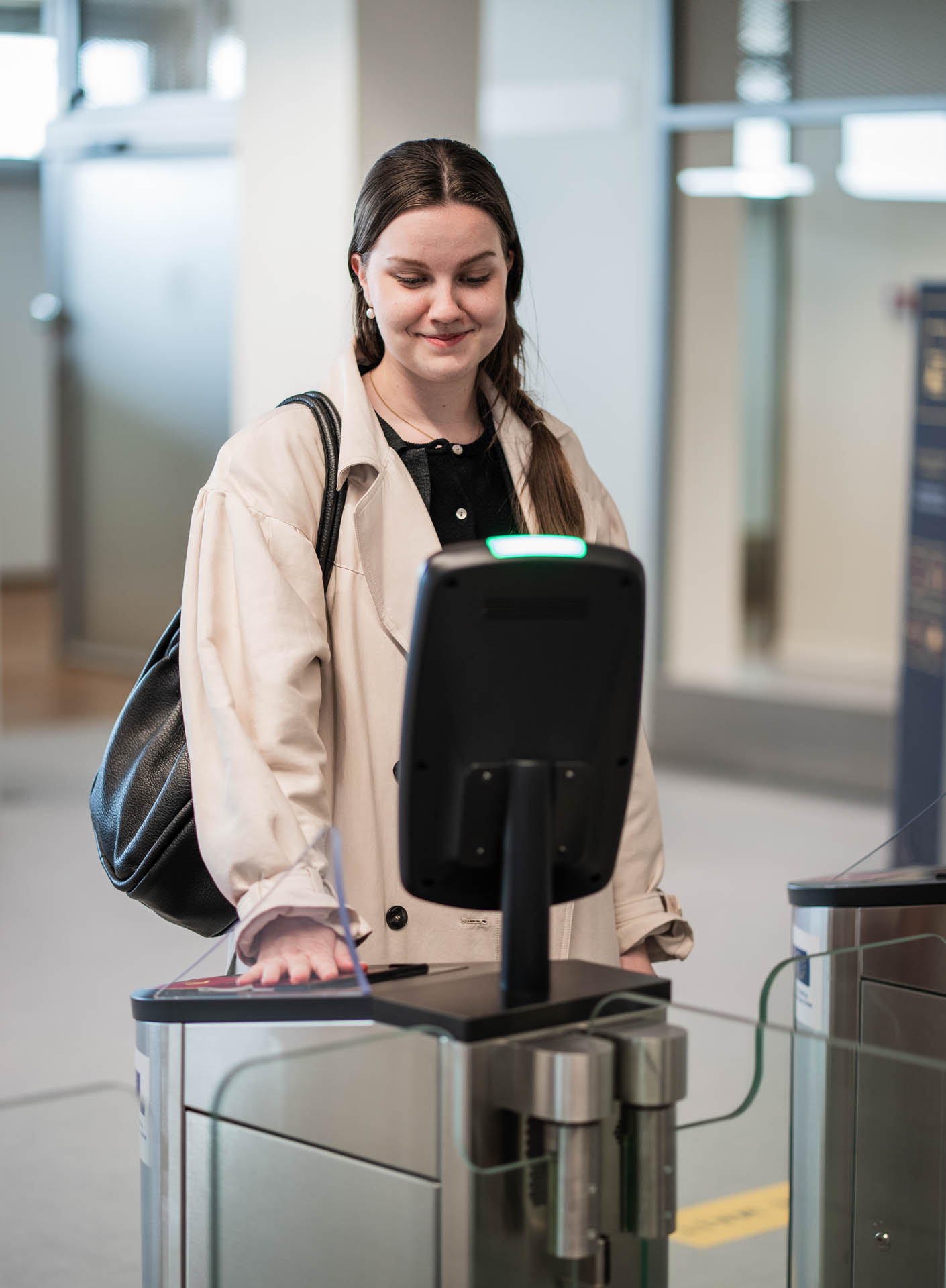 Woman using an automated biometric access gate, holding her smartphone at the scanner while the system verifies her entry.
